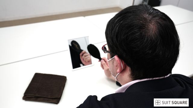 自分の頭皮を鏡でのぞき込む男性